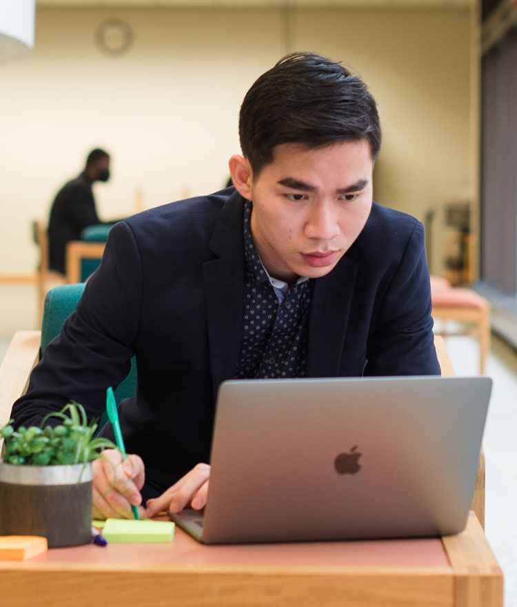 Student looking at a laptop and writing on a notepad