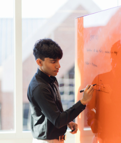 male student writing on orange whiteboard